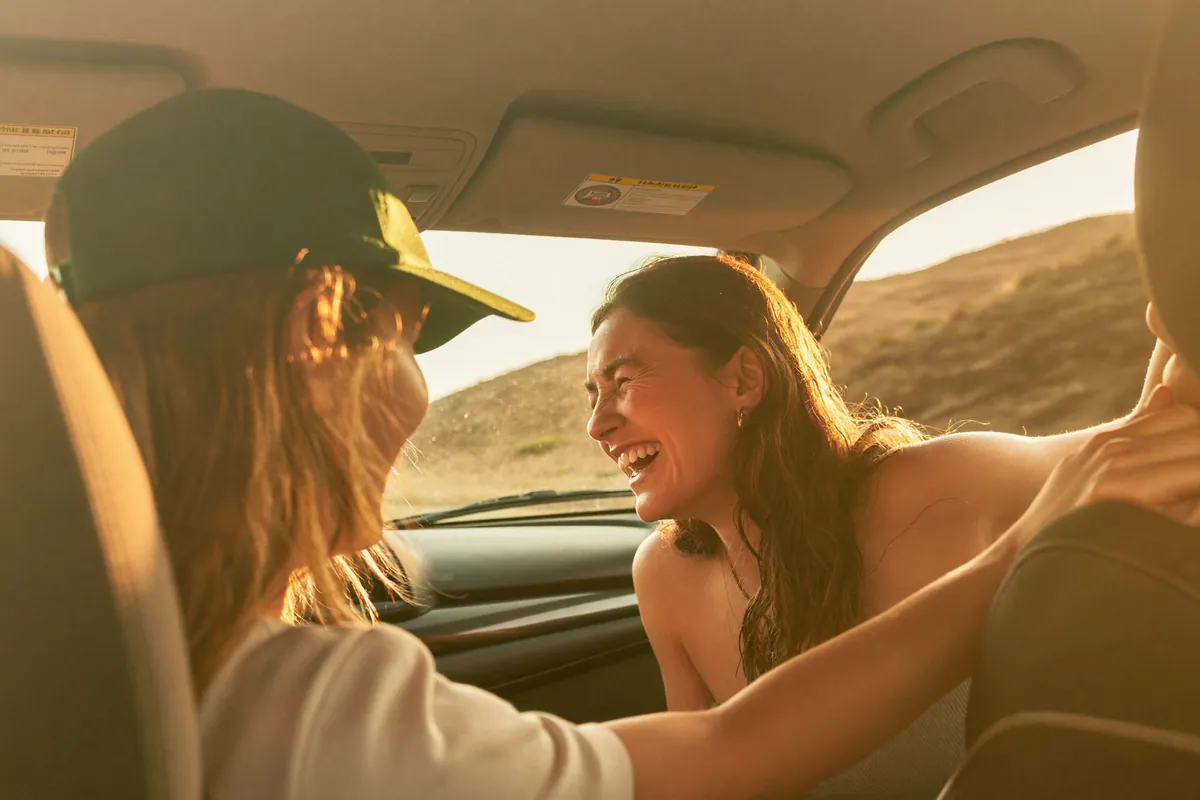 Deux amies rient dans une voiture sur une route de campagne